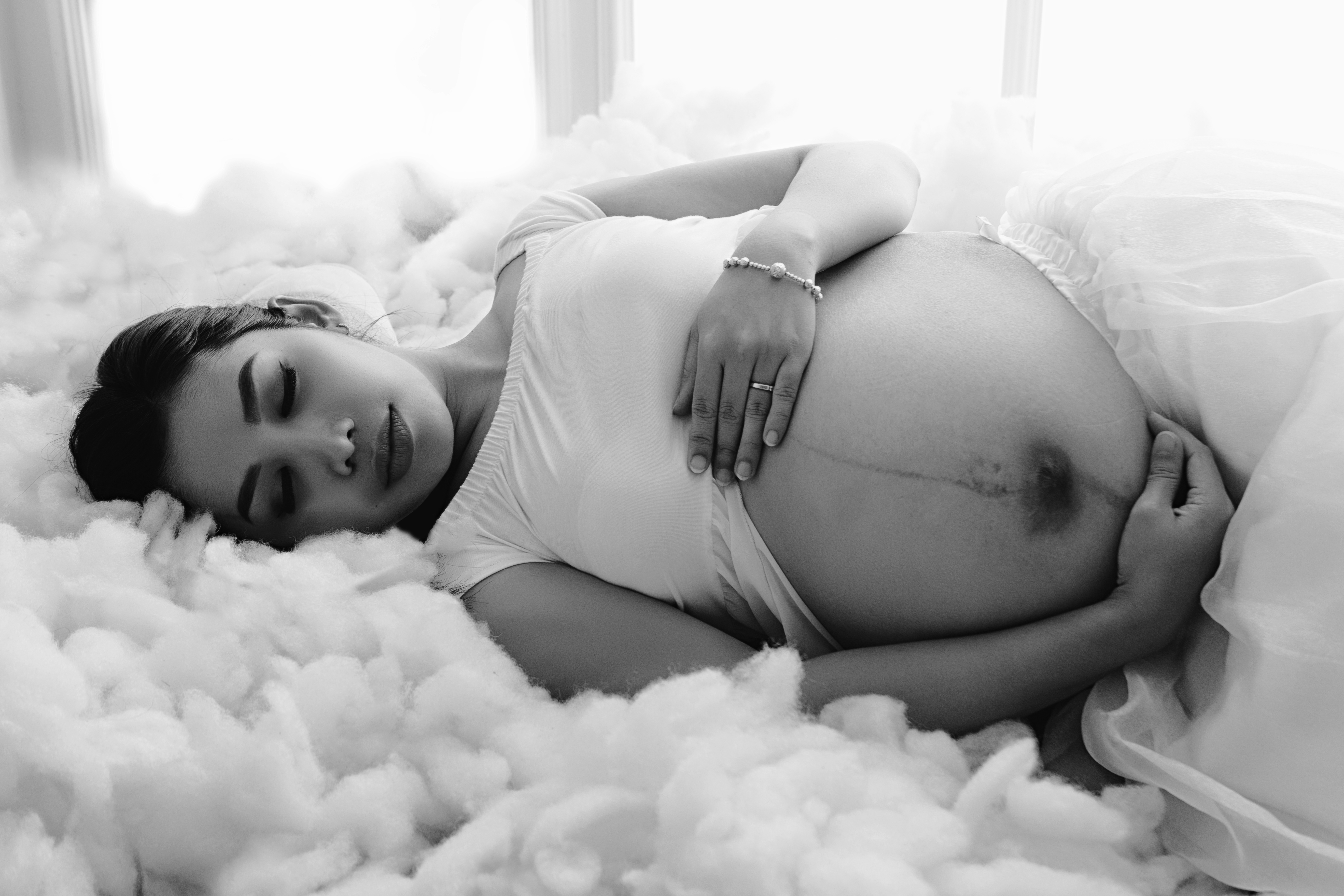 Expectant mother cradling her baby bump in a floral dress with soft backlighting